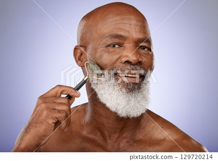 Skincare, face roller and old man facial massage with gua sha stone for glowing healthy skin. Wellness, dermatology and relax, portrait of black man with jade roller for anti aging routine in studio. 129720214