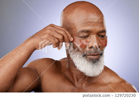 Skincare, eye patches and senior man doing wellness, health and natural face routine in studio. Cosmetic, beauty and elderly African guy doing self care facial treatment isolated by purple background Skincare, eye patches and senior man doing wellness, health and natural face routine in studio. Cosmetic, beauty and elderly African guy doing self care facial treatment isolated by purple background 129720230