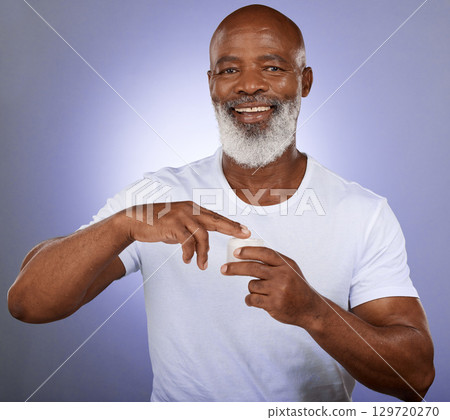 Black man, mature face and skincare cream on purple studio background for dermatology, healthcare wellness or collagen treatment. Portrait, smile or happy middle aged model with facial beard product 129720270