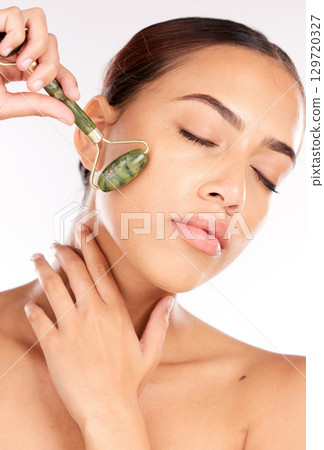 Face, beauty and skincare of woman with jade roller in studio isolated on a white background. Makeup, cosmetics and female model from Canada with eyes closed and facial roller for healthy smooth skin Face, beauty and skincare of woman with jade roller in studio isolated on a white background. Makeup, cosmetics and female model from Canada with eyes closed and facial roller for healthy smooth skin 129720327