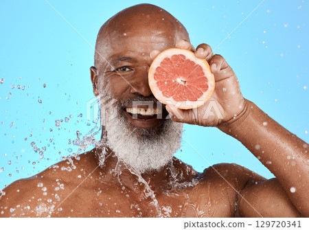 Portrait, skincare or black man with grapefruit studio with water splash on blue background with mockup space. Smile, face or senior male model on healthy diet for beauty, detox or vitamin c benefits 129720341