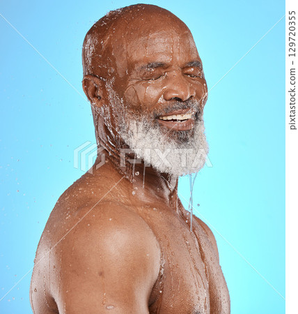 Water splash, skincare and face of senior black man in studio isolated on a blue background. Cleaning, hygiene and retired elderly male from Nigeria bathing or washing for wellness and healthy skin. 129720355