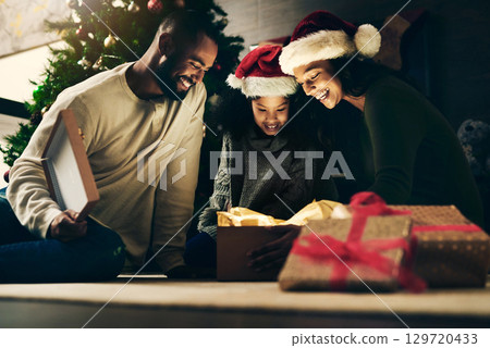 Mother, father and child with gift for Christmas in celebration of a Christian winter holiday as a happy family. Night, mom and dad love giving young girl a surprise present to celebrate xmas at home Mother, father and child with gift for Christmas in celebration of a Christian winter holiday as a happy family. Night, mom and dad love giving young girl a surprise present to celebrate xmas at home 129720433