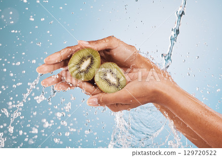Water splash, hands of woman and kiwi in studio on a blue background. Cleaning, hygiene and female model washing fruits for healthy diet, nutrition and vitamin c for skincare, beauty and wellness. 129720522