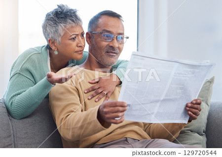 Senior couple, shocked and surprised by news while reading newspaper on sofa in living room at home together. Old man and woman check media article with fake news or bad crisis headline in retirement 129720544