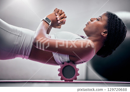 Yoga, floor and black woman with foam roller for massage, healthcare or back support help in health club, studio or gym. Muscle relief, sports wellness and neon pilates athlete doing fascia exercise 129720688