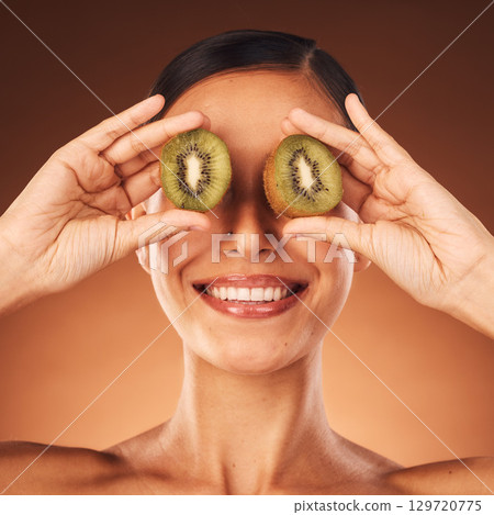 Face beauty, skincare and woman with kiwi in studio isolated on a brown background. Food, cosmetics and happy female model with fruit for healthy diet, wellness or vitamin c, nutrition or facial care 129720775