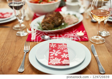 Wine glass, plate and cutlery on the table at a christmas party or event in the dining room of a house. Napkin, table setting and dinner party for a festive xmas holiday lunch celebration at a home. 129720839