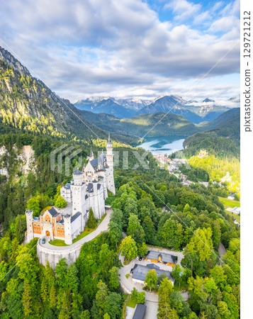 Neuschwanstein Castle stands majestically amidst lush forests and mountains in Bavaria. The clear sky enhances the picturesque beauty of this fairy-tale structure surrounded by nature. 129721212