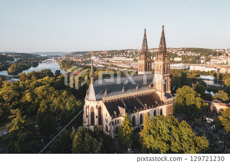 Vysehrad Basilica of St. Peter and St. Paul stands majestically in Prague during sunrise. The church is surrounded by lush greenery and overlooks the river, creating a serene atmosphere. 129721230