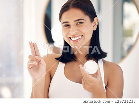 Face, beauty and skincare with a woman in the bathroom of her home to promote a cosmetic product. Portrait, antiaging and treatment with an attractive young female applying lotion to her skin 129721235