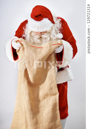 Santa Claus, bag and gift with a man in a costume posing in studio on a gray background for the holidays. Delivery, Father Christmas and sack with a male in an outfit for festive season celebration 129721314