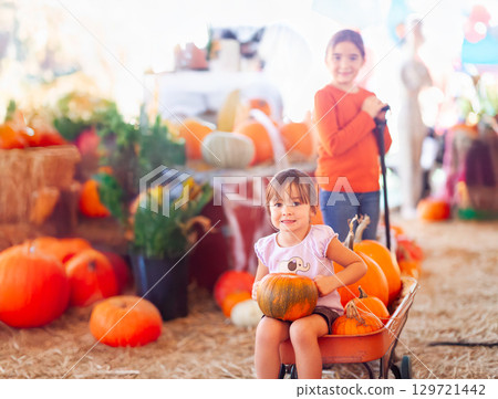 Two Sisters Enjoying a Wagon Ride at a Pumpkin Patch on a Fall Day. 129721442