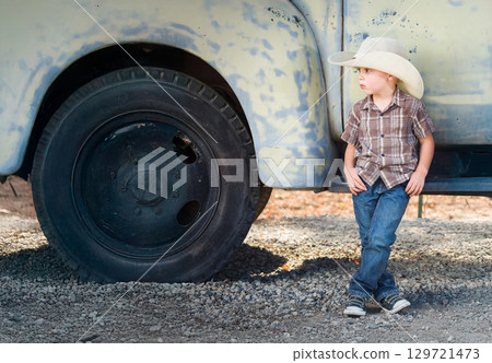 Young Boy Wearing Cowboy Hat Relaxing Leaning Against Antique Truck. Young Boy Wearing Cowboy Hat Relaxing Leaning Against Antique Truck. 129721473