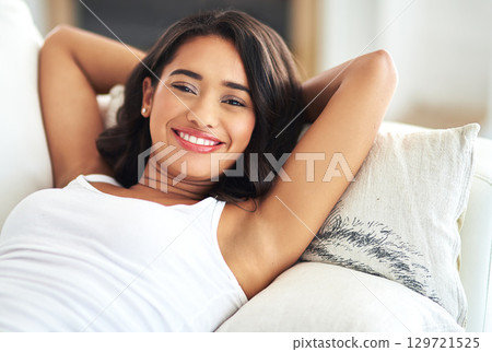 Portrait, relax and happy with a black woman lying on a sofa in the living room of her home over a weekend. Face, smile and rest with a young female chilling in a house with hands behind her head Portrait, relax and happy with a black woman lying on a sofa in the living room of her home over a weekend. Face, smile and rest with a young female chilling in a house with hands behind her head 129721525