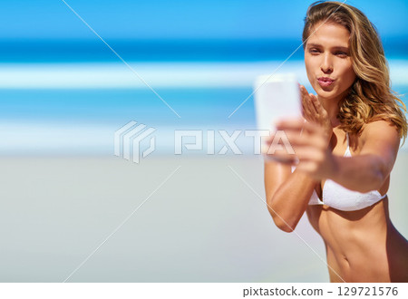 Woman, phone selfie and beach vacation while blowing kiss for influencer social media page for travel, holiday and motivation outdoor. Female at sea for summer bikini body inspiration in nature 129721576