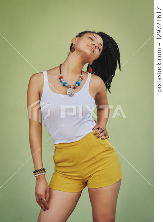 Young black woman, fashion and style with jewelry, trendy and colorful necklace with confident pose against green studio background. African model with cosmetic jewellery and stylish mock up. 129721617