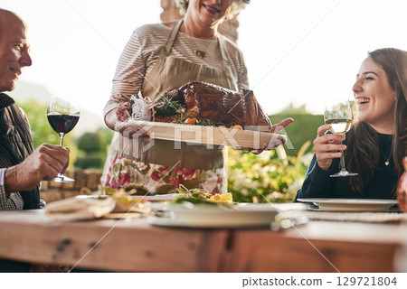 Thanksgiving, food and family with a woman carrying a turkey during a dinner party outdoor for celebration. Christmas, eating and tradition with a man and woman group enjoying chicken together 129721804