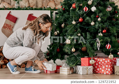 Christmas, gift by tree and holiday celebration with woman, decoration, festive box and tradition at family home. Presents under the Christmas tree, celebrate and packing, ornament and creative. Christmas, gift by tree and holiday celebration with woman, decoration, festive box and tradition at family home. Presents under the Christmas tree, celebrate and packing, ornament and creative. 129721952