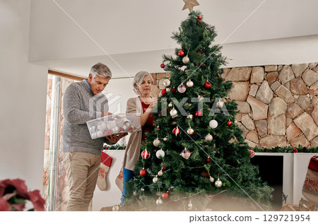 Elderly couple, Christmas and decorating tree together in preparation for the festive season at home. Senior man and woman hanging light or decor getting ready for the December holiday celebrations 129721954