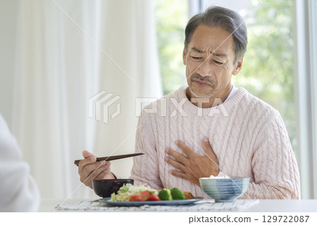 Senior man holding his hand around his stomach at the dinner table 129722087