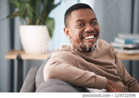 Face, smile and portrait of a black man relax in a living room at a house on a holiday, break or weekend. Happiness, calm and young male sitting alone in a lounge in home or apartment relaxing 129722096