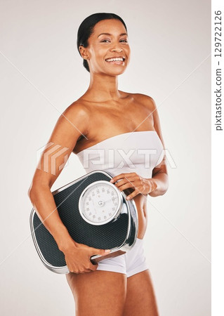 Fitness, portrait or woman with a scale in a studio for body goals, lose weight or health journey. Smile, results or happy young female model after training in workout isolated by a white background 129722126