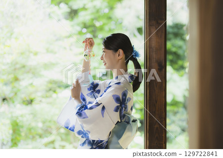 一個穿著浴衣的女人在門廊上拿著風鈴 129722841