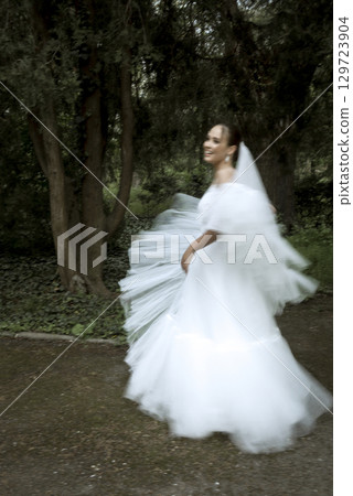 A bride in a white dress and a long veil stands among the trees A bride in a white dress and a long veil stands among the trees 129723904