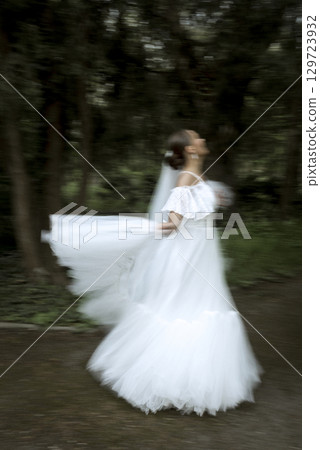 a bride in a white dress and a long veil stands among the trees a bride in a white dress and a long veil stands among the trees 129723932