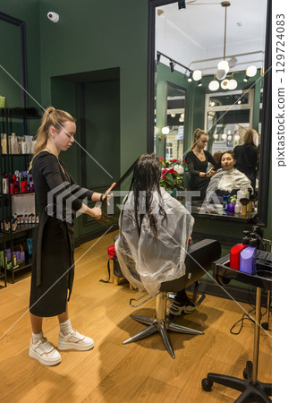 In a beauty salon, a girl client is having her hair styled and cut 129724083
