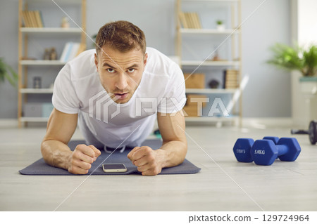 Young attractive man doing plank exercise lying on yoga mat on the floor at home. 129724964