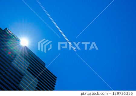 A passenger plane and contrails flying over a high-rise apartment building 129725356