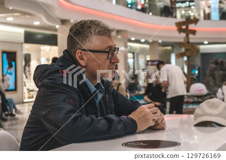man sitting thoughtfully in busy shopping mall while observing surrounding activity. man sitting thoughtfully in busy shopping mall while observing surrounding activity. 129726169