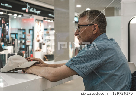 man sits waiting for an order in cafe in modern shopping mall in afternoon. close-up. man sits waiting for an order in cafe in modern shopping mall in afternoon. close-up. 129726170