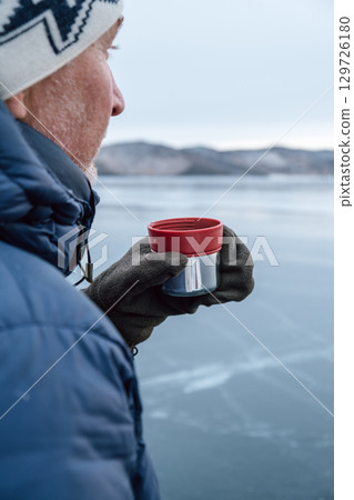 middle-aged man enjoys hot tea on frozen lake during winter chill. closeup. 129726180