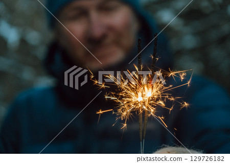 man igniting sparklers outdoors during winter evening celebration in snowy landscape. closeup. 129726182