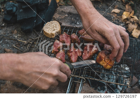 cooking meat over an open fire while camping in wooded area during autumn. closeup. 129726197