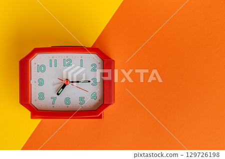 colorful alarm clock against vibrant orange and yellow background creates lively atmosphere. closeup colorful alarm clock against vibrant orange and yellow background creates lively atmosphere. closeup 129726198