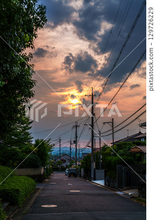 The cityscape illuminated by the setting sun peeking through the clouds, the sun painting the sky and city golden The cityscape illuminated by the setting sun peeking through the clouds, the sun painting the sky and city golden 129726229