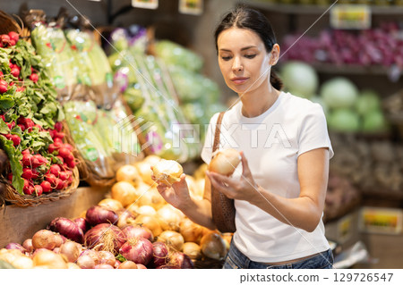 Girl client near vegetable stand in store choose onion Girl client near vegetable stand in store choose onion 129726547