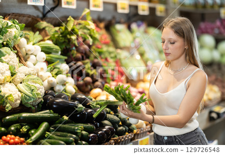 Girl client near vegetable stand in store choose bunch of green onion Girl client near vegetable stand in store choose bunch of green onion 129726548