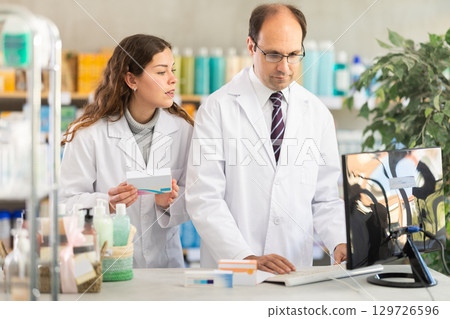 Experienced pharmacist and his assistant check data on medical drugs on Internet 129726596