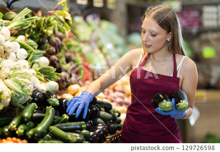 Female grocery store worker offers ripe zucchini in grocery department of supermarket Female grocery store worker offers ripe zucchini in grocery department of supermarket 129726598