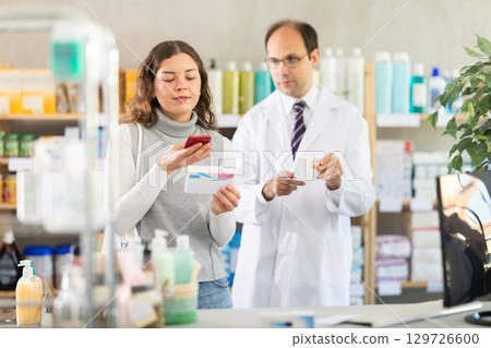 Experienced pharmacist and his assistant check data on medical drugs on Internet 129726600