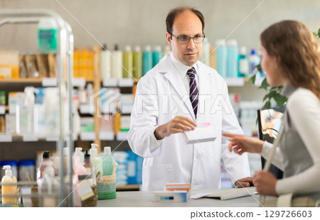 Experienced male pharmacist helping girl choose medicines in pharmacy 129726603