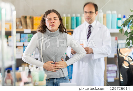 Woman suffering from stomach pain. Male pharmacist offering stomach pain pills 129726614