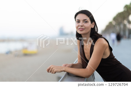 Young woman is leaning on parapet, looking towards sea. 129726704