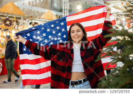 Happy girl with flag of United States at city Christmas market Happy girl with flag of United States at city Christmas market 129726705