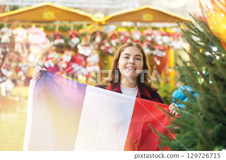 Smiling girl with flag of France walking on street Christmas fair 129726715